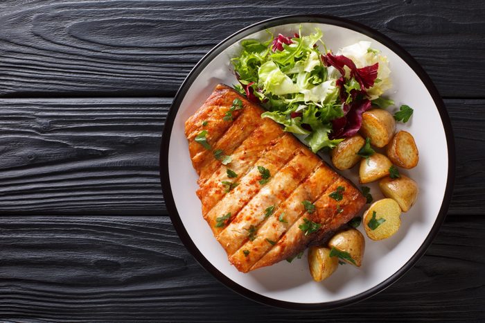 Healthy lunch grilled swordfish fillet with fried potatoes and fresh salad close-up on a plate on a wooden table. horizontal top view from above