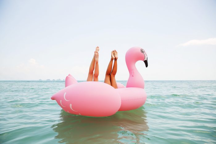Summer lifestyle funny image of two pretty girls friends having fun on air mattress in the ocean. Doing yoga and having fun. Legs up in the air. Positive emotions, bright colors