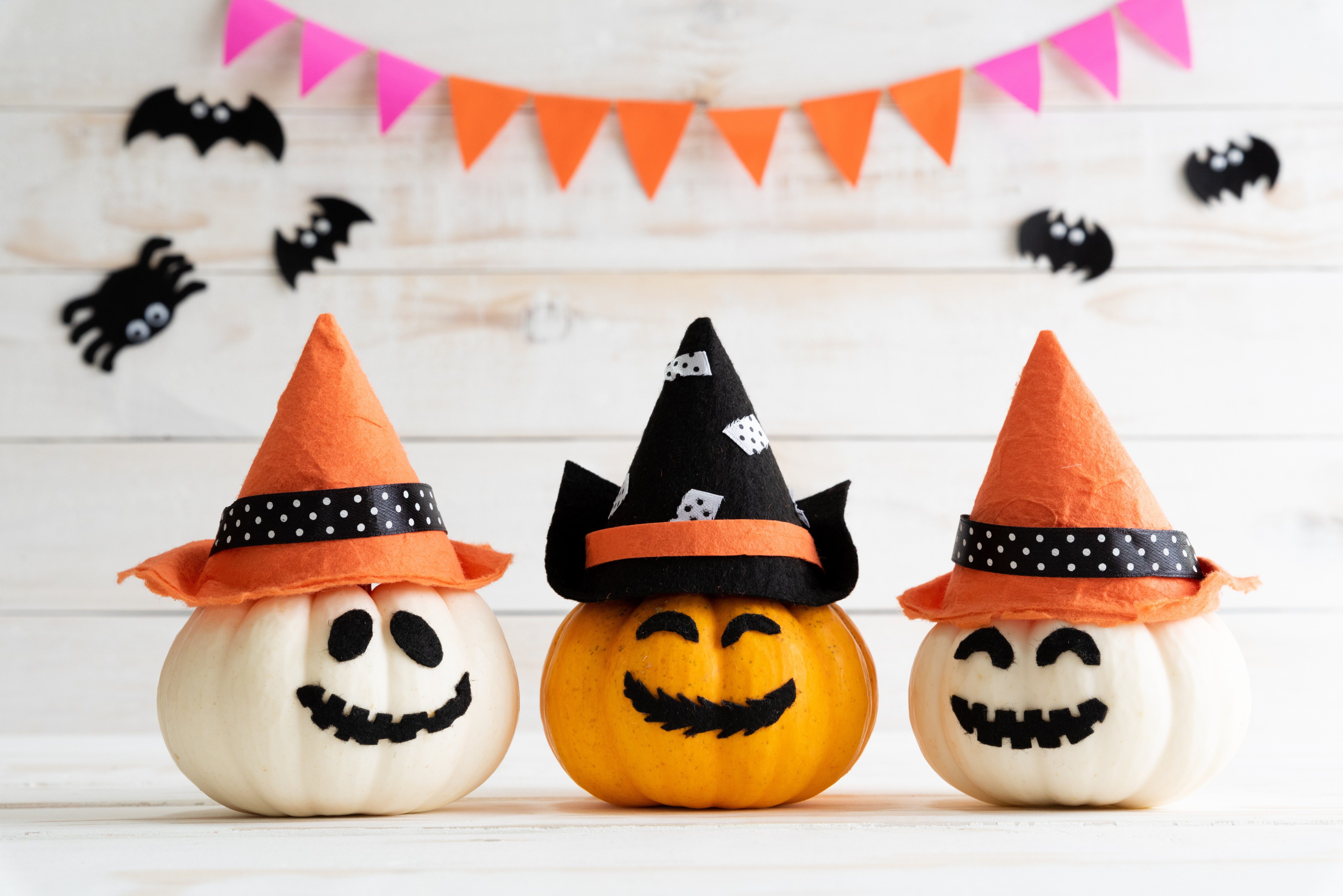 White and yellow ghost pumpkins with witch hat on white wooden borad background with bat. halloween concept.