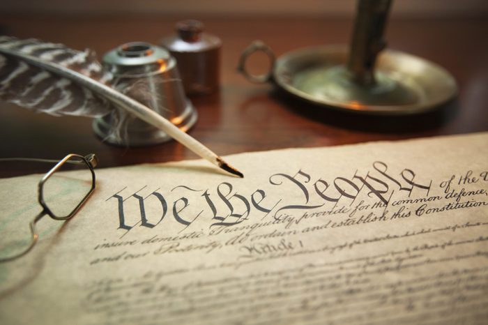 Selective focus image of the United States Constitution with quill pen, glasses and candle holder