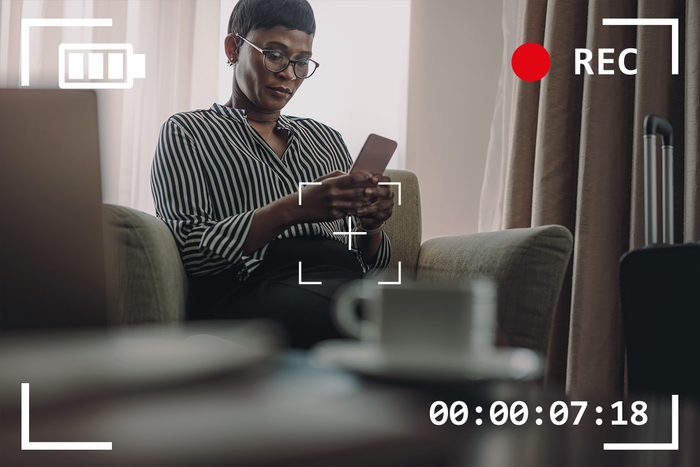 woman using smartphone while sitting in hotel room with camera viewfinder overlay