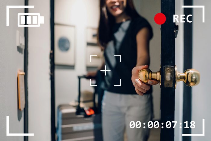 woman opening door holding suitcase with camera viewfinder overlay