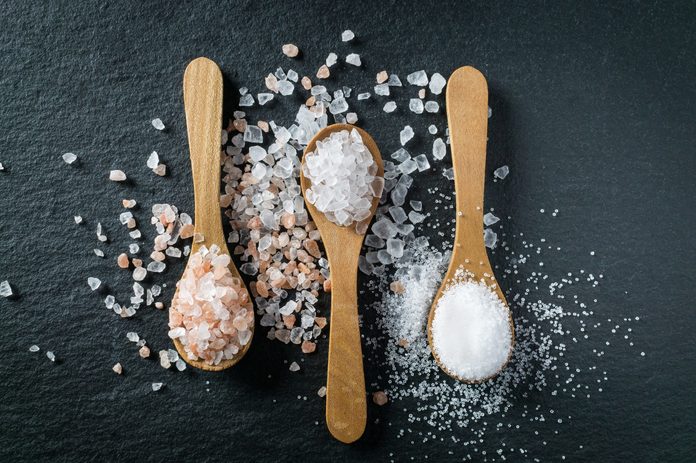 Different types of salt. Sea, himalayan and kitchen salt. Top view on three wooden spoons on black background