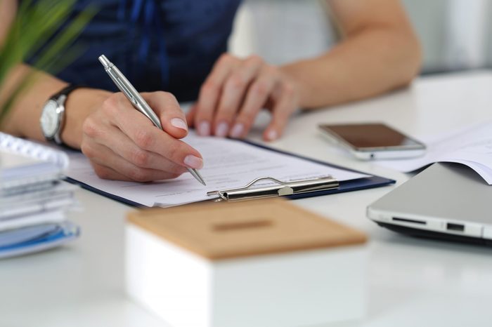 Close-up of female hands. Woman writing something and looking at mobile phone screen sitting at her office