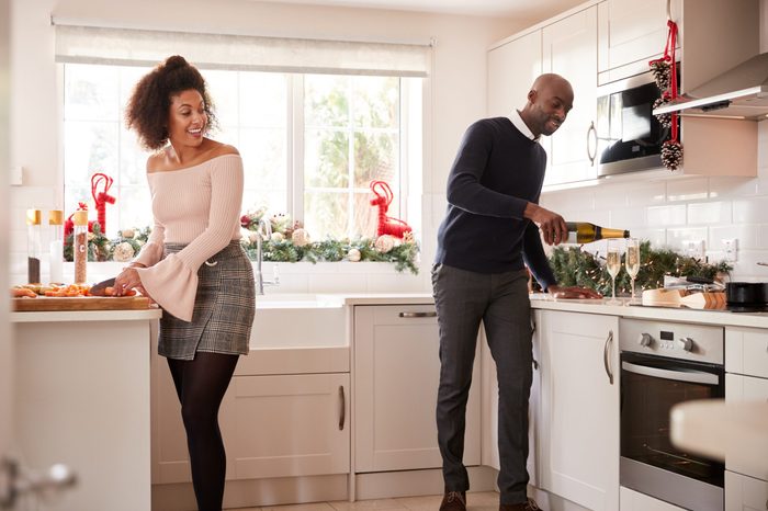 Young mixed race couple preparing Christmas dinner in the kitchen, the man pouring glasses of champagne