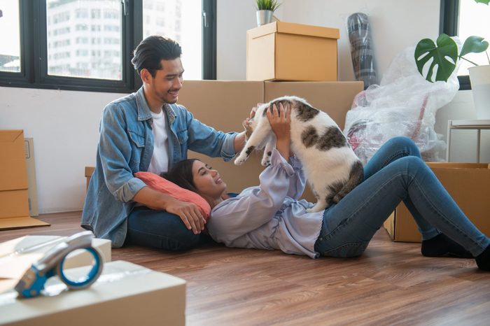 Young Asian couple or family feeling happy relaxing and play with their cat after moving to new house or apartment.