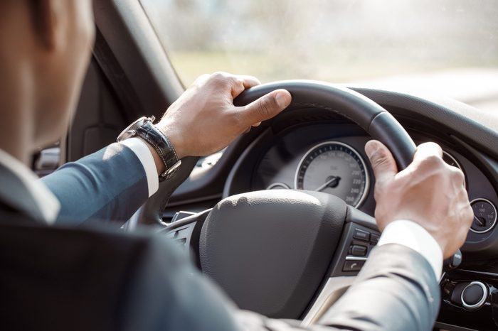 Young black businessman driver wearing expensive watch sitting inside the car driving holding steering wheel close-up back view