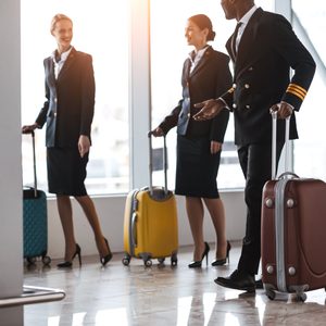 pilot and stewardesses with luggage walking by airport