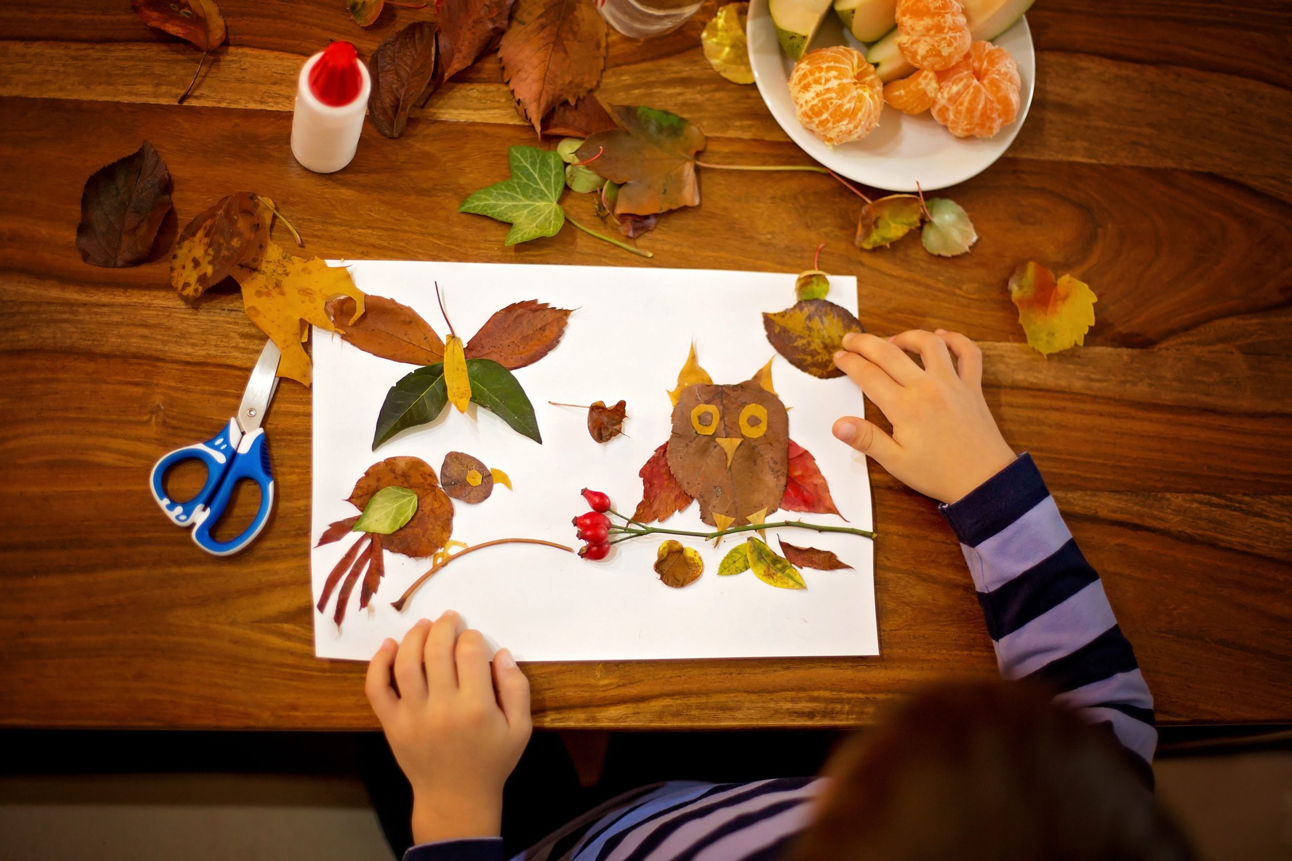 Sweet child, boy, applying leaves using glue while doing arts and crafts in school, autumn time