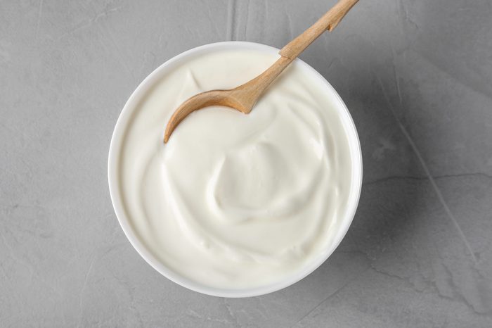 Bowl of sour cream with wooden spoon on grey table, flat lay