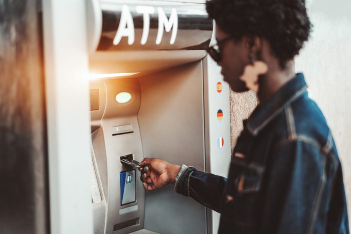 Side view of an African female withdrawing the money from a bank card using street ATM machine; a black girl is inserting her bank card into an automated teller machine to replenish her account