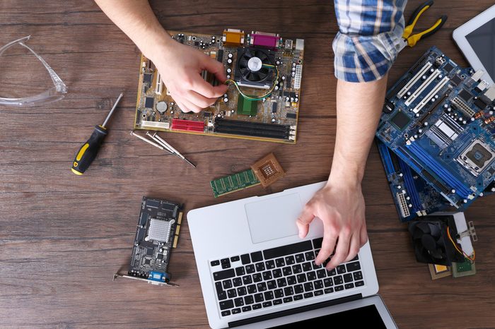 Male hands repairing computer details and using laptop on wooden table, top view