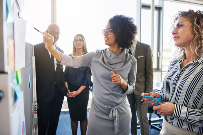 Diverse group of focused businesspeople brainstorming together on a whiteboard during a strategy session in a bright modern office