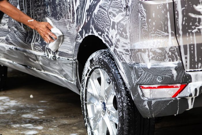 Manual car wash in car wash shop service with employee worker in back.