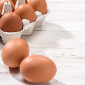 Close-up view of raw chicken eggs in egg box on white wooden background