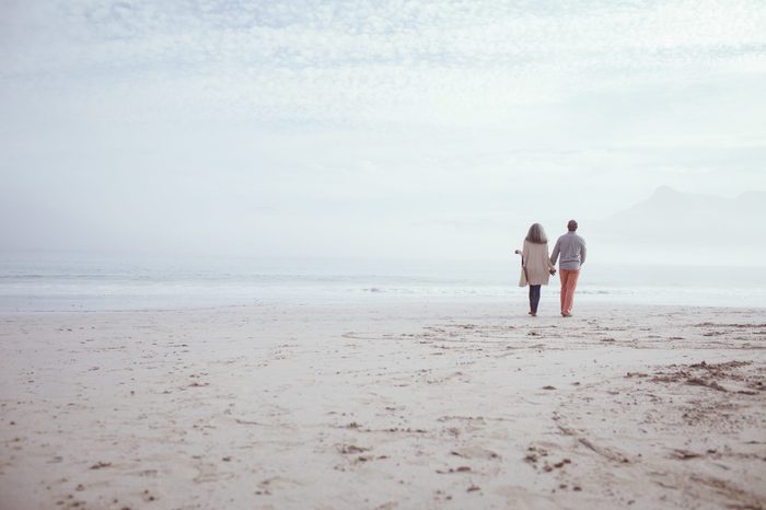 Rear view of happy senior African-American couple walking hand in hand on beach on beautiful day. Authentic Senior Retired Life Concept