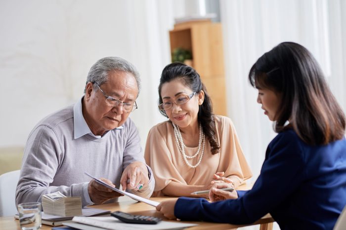 Loving senior couple sitting at spacious office of estate agent and asking questions concerning terms of purchase agreement