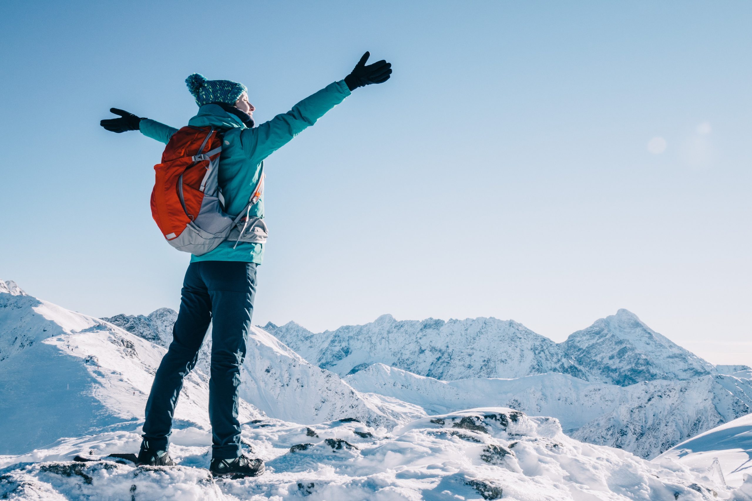 Hiker woman standing with hands up achieving the top, admiring winter mountain landscape. Happy tourist woman in winter. High Tatras, 1987 meter above sea level. Poland, Slovakia