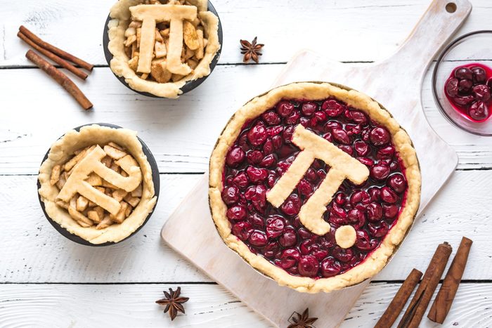 Pi Day Cherry and Apple Pies - making homemade traditional various Pies with Pi sign for March 14th holiday, on white wooden background, top view.