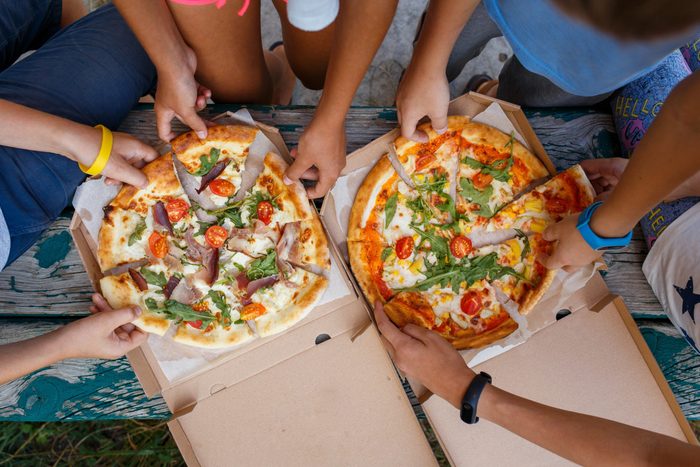 Top view image of children grab slices of pizza from box at the outdoors picnic. Children hands taking pizza