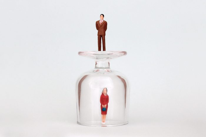 A miniature woman in a glass cup and a miniature man on top of a glass cup. The concept of the gender promotion gap.