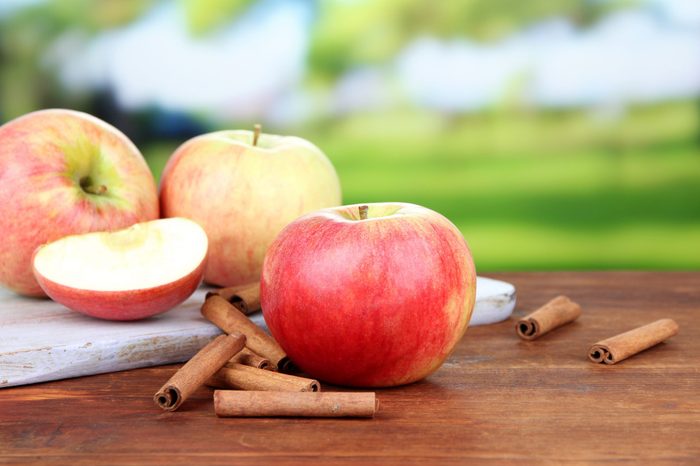 Ripe apples with cinnamon sticks on wooden table, on bright background