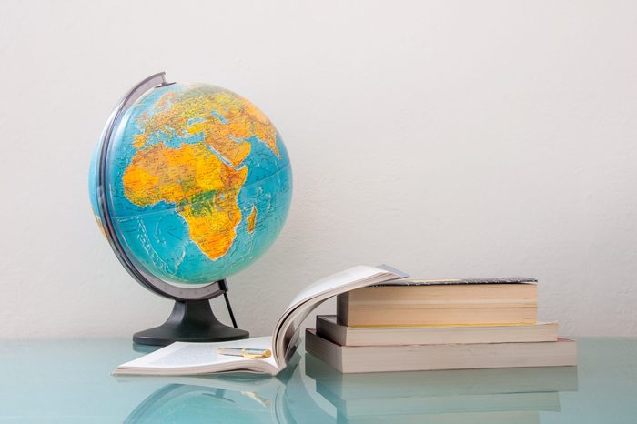 desk with a pile of books and school supplies like pencils and stationery and world map globe, back to school college university education concept, homework classroom study