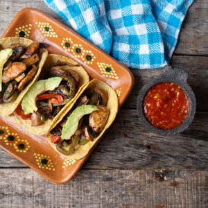 Mexican vegan tacos with avocado and mushrooms on wooden background