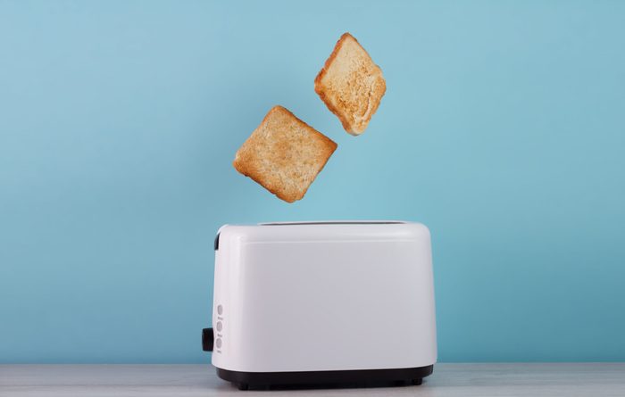 Roasted toast bread popping up of stainless steel toaster on a blue backgroun.Space for text