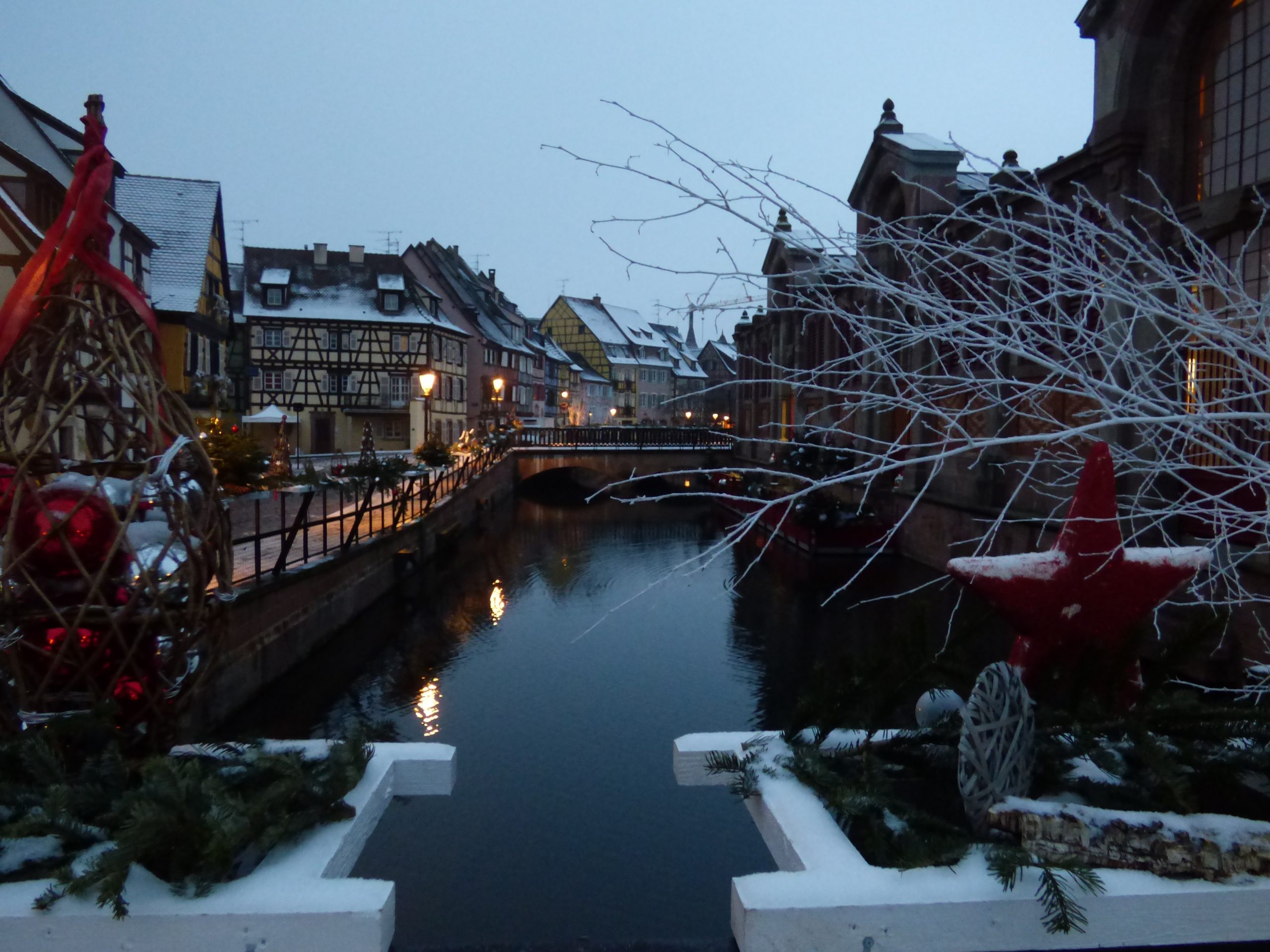 Christmas decorations : red balls, wooden red star, fir branches, fresh snow.Sunrise, streets lights, Colmar, Alsace, France.Can be used for editorial and commercial purposes.