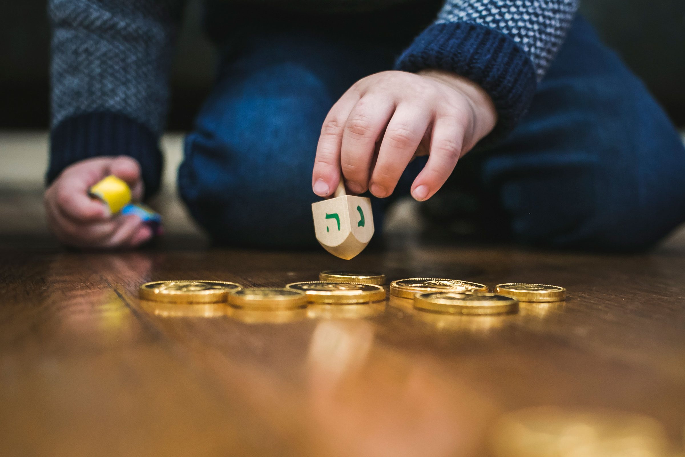 close up of young boy playing with a dreidel and hanukkah gelt on the floor