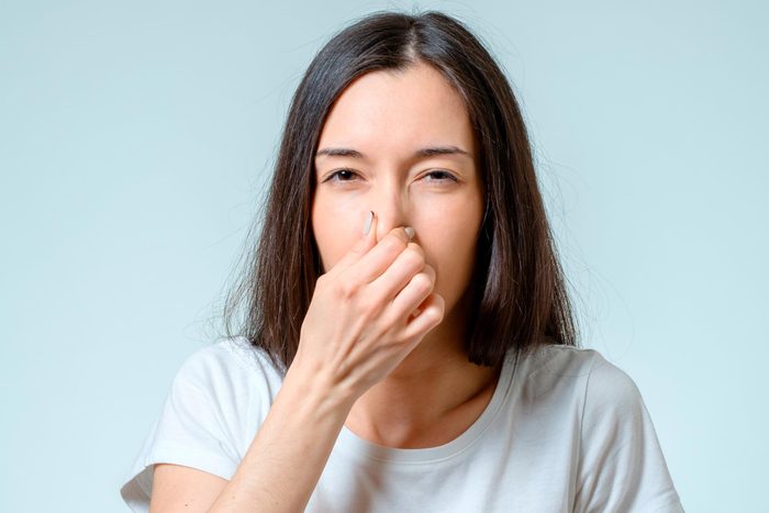 Girl covers nose with hand showing that something stinks isolated on gray background