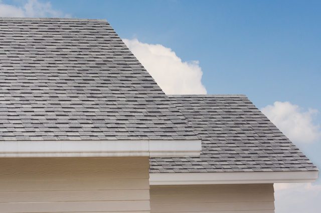 Roof shingles on top of the house against blue sky with cloud, dark asphalt tiles on the roof background.