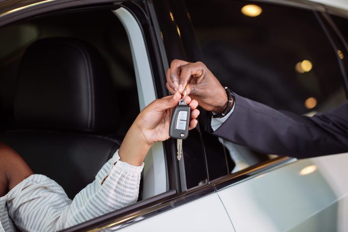 Young car african female salesman giving a key from the new car to the beautiful young african couple owners