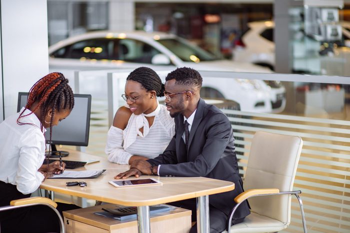 Beautiful young couple signs documents at dealership showroom.