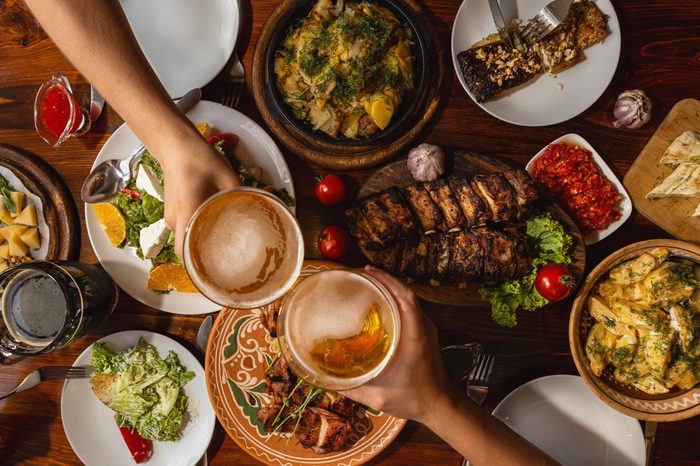 a large wooden table generously covered with delicious national dishes, with friends sitting and drinking light beer from glasses