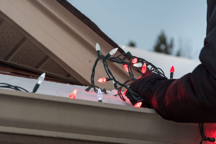 Close up of arms hanging a tangled pile of red and white Christmas lights on a snow covered roof.