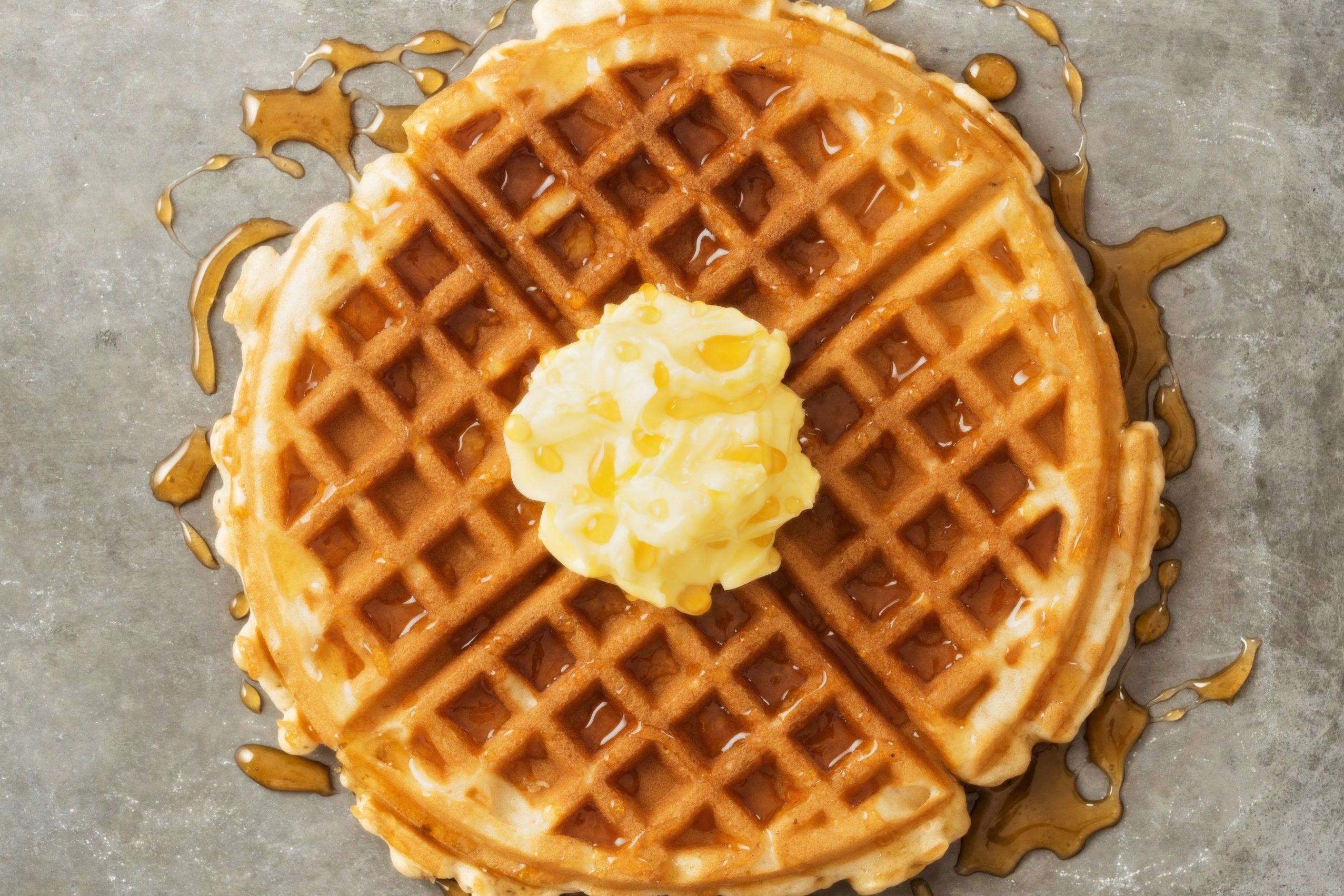 close up of rustic traditional waffle with butter and maple syrup