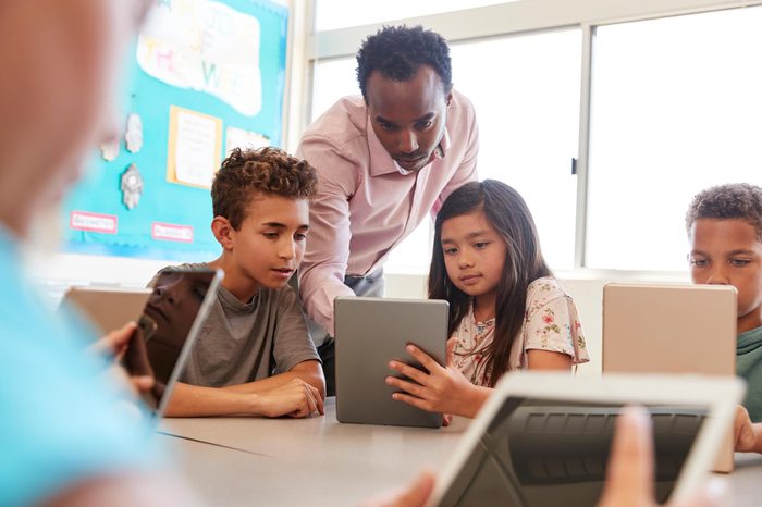 teacher among kids using tablets computers in the classroom at school