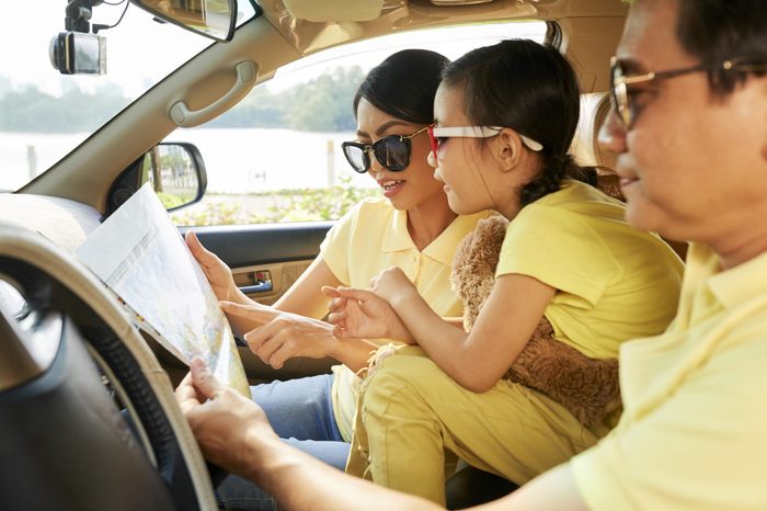 Mature Vietnamese man with his wife and daughter sitting in car and searching destination point on a map