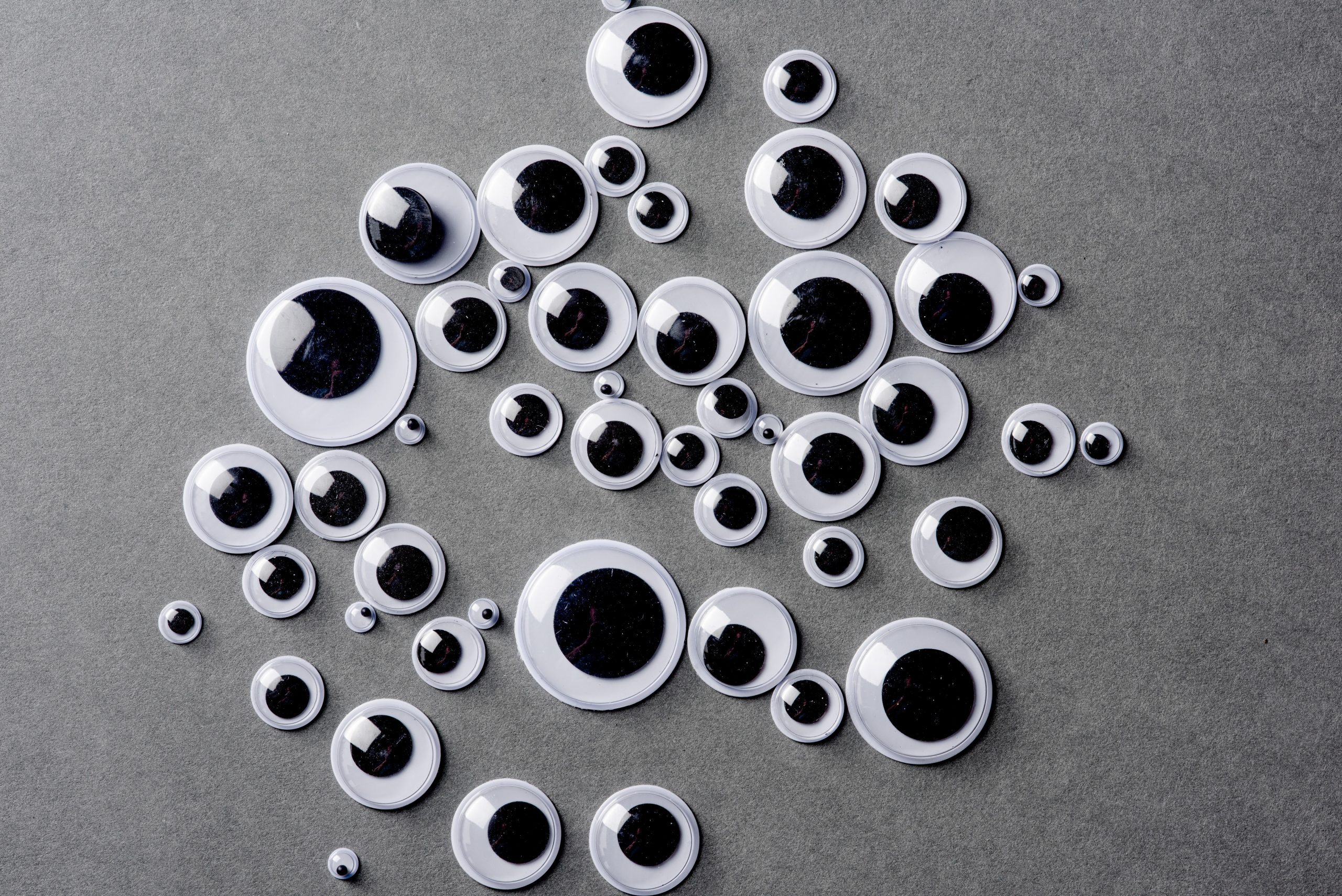 Many different sizes of googly eyes on grey background.