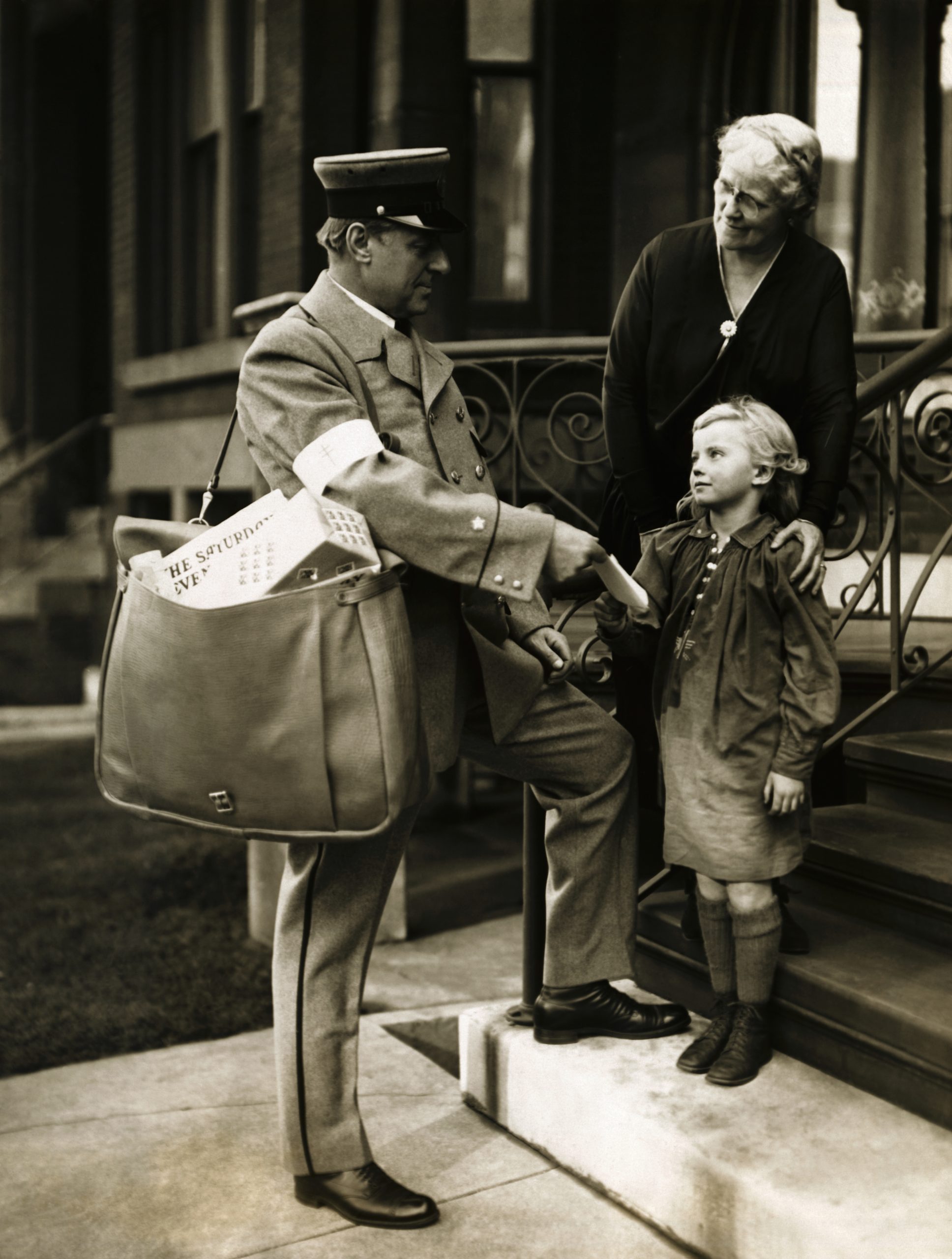 Deserting his desk in the Federal Building, Postmaster Arthur C. Leuder garbed himself in a regulation mail carrier's uniform, borrowed a mail pouch from one of his men, and personally delivered the first Christmas Sealed letter opening the 1925 campaign to raise funds to fight tuberculosis. Photograph shows Postmaster Leuder delivering the first Christmas Sealed letter to Miss Elizabeth Alexander, 6, and her grandmother Mrs. Edward P. Martin at their home at 27 Scott Street.