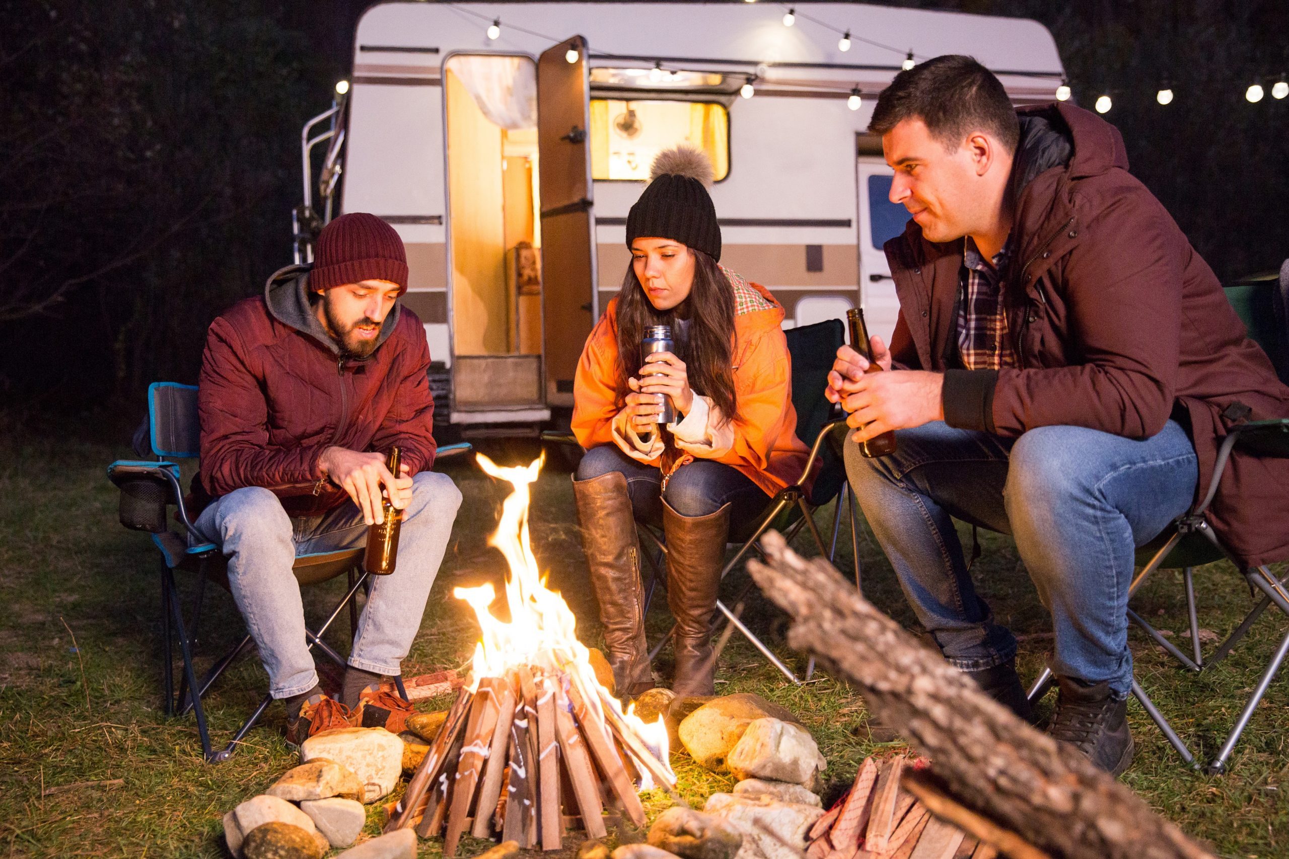 Close friends sitting together on camping chairs around camp fire in the mountains. Retro camper van.