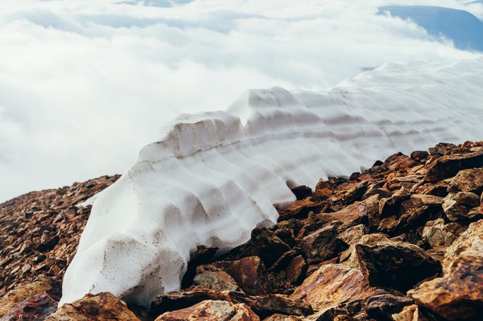 Large snowy dome on mountain top close-up. Firn on stony mountain peak on background of clouds. Snow on mountain on high altitude. Atmospheric minimalist alpine landscape. Wonderful highland scenery.