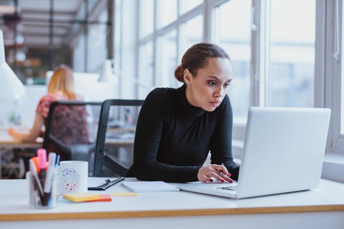 Image of woman using laptop while sitting at her desk. Young african american businesswoman sitting in the office and working on laptop.