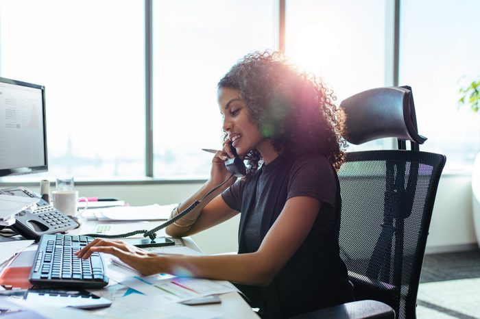 Woman entrepreneur busy with her work in office. Young woman talking over telephone while working on computer at her desk.