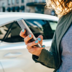 Female's hands holding mobile device in city, close-up.