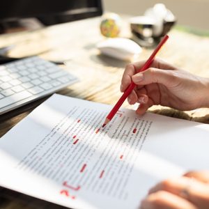 Close-up Of A Person's Hand Marking Error With Red Marker On Document