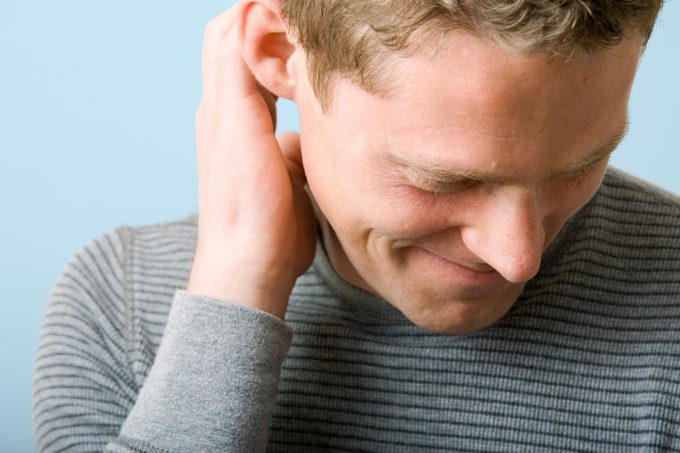 portrait of a man scratching his ear looking down. blue-gray background