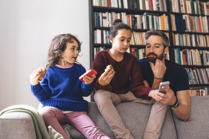 bearded father and two daugthers on sofa looking at devices